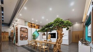 Een modern interieur met een centrale houten tafel, stoelen en een grote boomsculptuur.