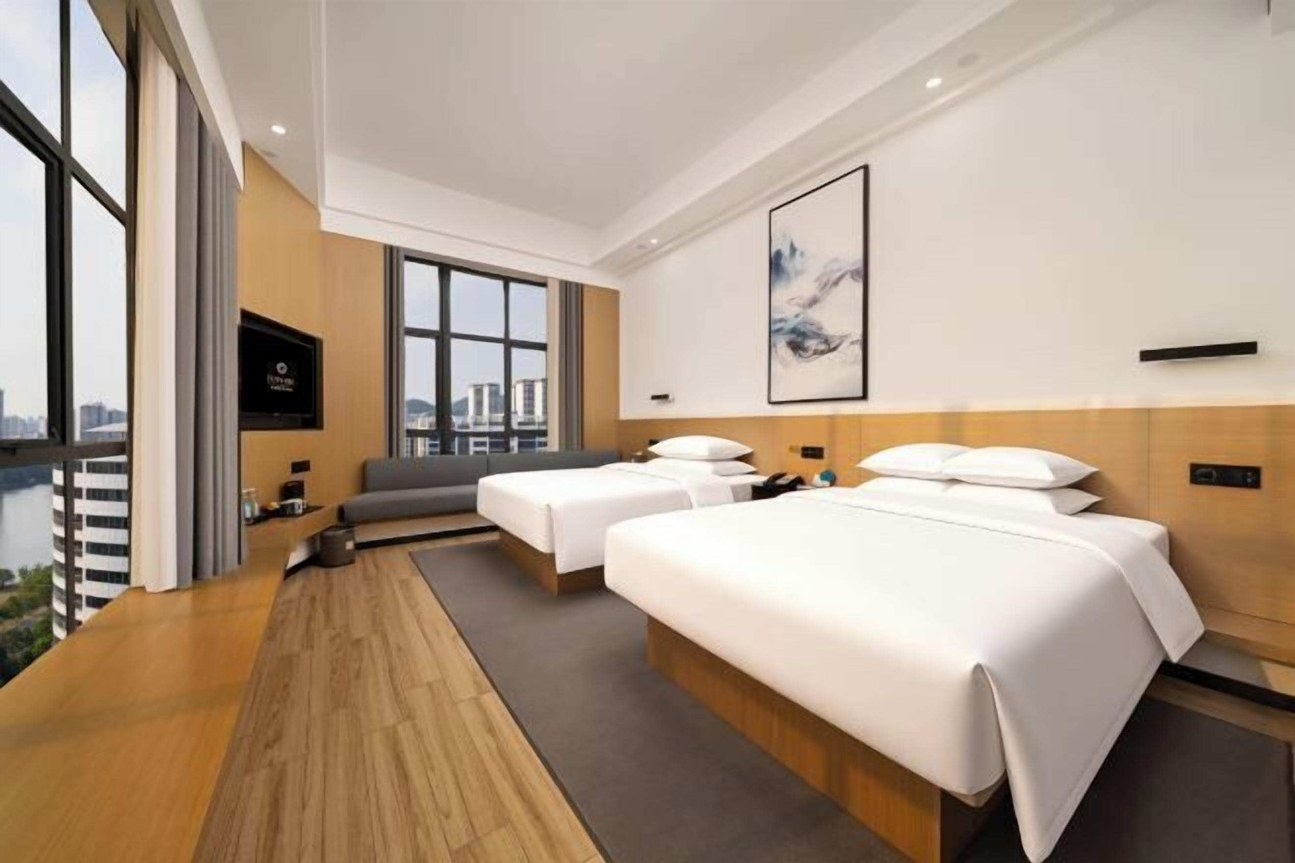A hotel room with two beds, a sofa, a TV, and a large window with a city view.