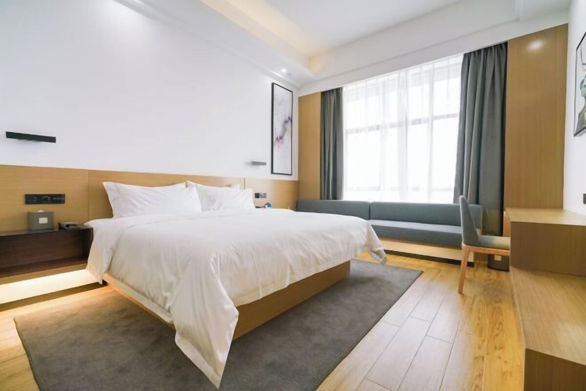 Una habitación de hotel moderna con una cama grande, un escritorio, un sofá y una ventana con cortinas.