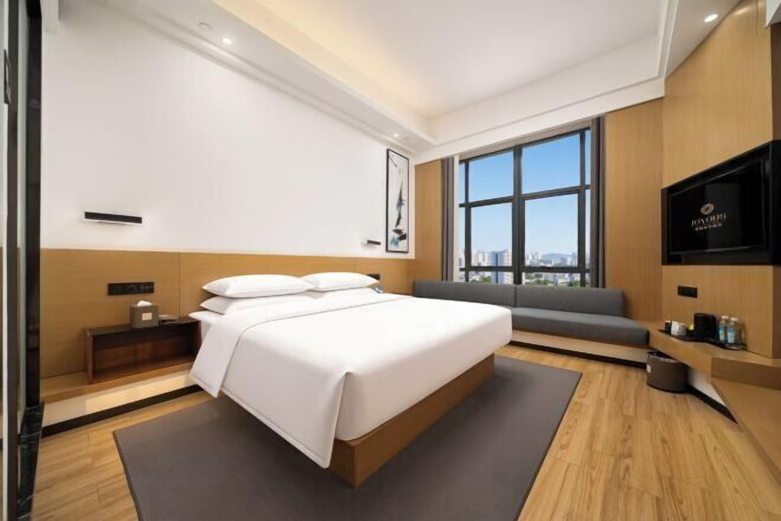 A modern hotel room with a large bed, a sofa, a TV, and a city view.