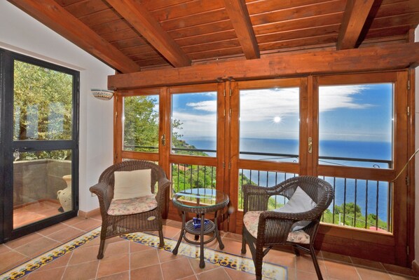 Un balcon avec des fauteuils en osier, une petite table et une vue sur la mer.