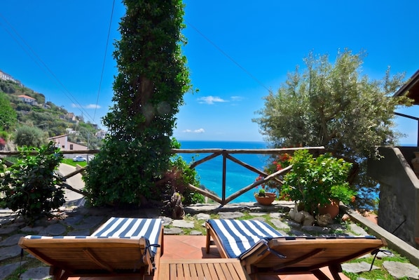 A terrace with two lounge chairs, a view of the sea, and a stone pathway.