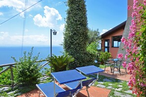Une terrasse avec des tables de ping-pong, une haute haie verdoyante et une vue sur la mer.