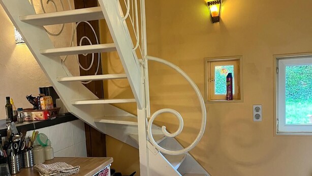Una cocina con una escalera espiral blanca, una ventana pequeña y una lámpara fijada a la pared.