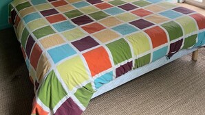Un dormitorio con colcha de patchwork colorida, techo de madera y pared verde azulada.