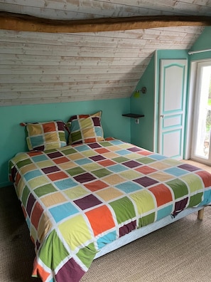 Une chambre avec une couvre-lit matelassé aux couleurs vives, un plafond en bois et un mur de couleur turquoise.