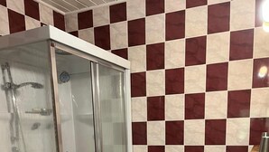 Un baño con cabina de ducha de vidrio, tocador de madera con un lavamanos grande y pared de baldosas a cuadros.