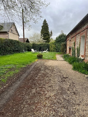 Une allée de gravier mène à une maison dont la façade est en briques et qui est entourée d’une pelouse verte.