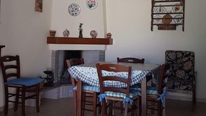 A dining area with a round table, six chairs, a hanging light fixture, a fireplace, and wall decorations. - House / Villa - Villasimius (Villasimius)