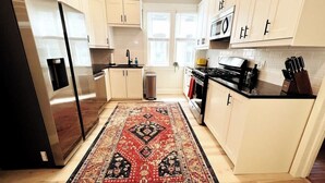 A modern kitchen with light-colored cabinets, a stainless steel refrigerator, a microwave, and a stove. - Trendy and Stylish 3BR Uptown Unit (Minneapolis)