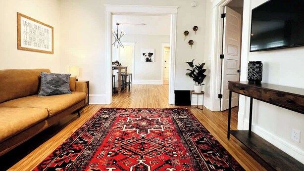 A living room with a brown sofa, a red patterned rug, a TV on the wall, and a wooden coffee table. - Trendy and Stylish 3BR Uptown Unit (Minneapolis)