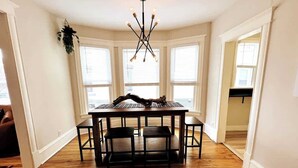 A dining area with a wooden table and chairs, a chandelier, and large windows. - Trendy and Stylish 3BR Uptown Unit (Minneapolis)