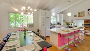 Une cuisine moderne dotée d’un îlot central, de meubles blancs et d’un coin repas avec une longue table dressée pour quatre personnes.