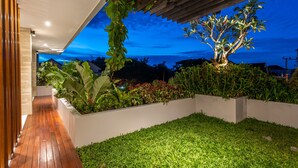 Un patio moderno al aire libre con piso de madera, césped cuidado y diversas plantas y flores.