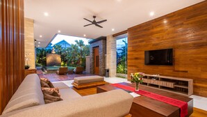 Una sala de estar moderna con un sofá grande, detalles de madera, un televisor y vistas al exterior.