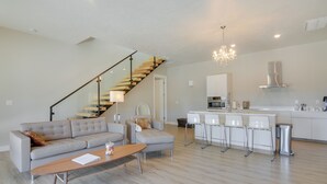 A modern living room with a staircase, a dining area, and a kitchen.