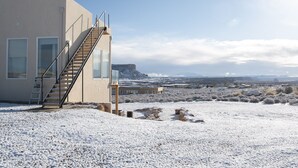 A modern building with a staircase leading to a balcony, surrounded by a snowy landscape and distant mountains.