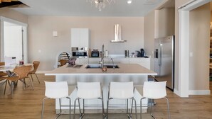 A modern kitchen with a central island, white bar stools, and a chandelier.