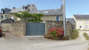 A stone house with a grey door, a stone wall, and a flower bed with pink flowers.
