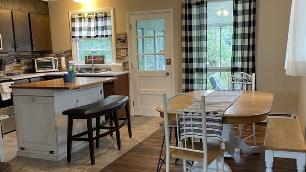 A kitchen with a wooden island, a dining table with chairs, a ceiling fan, and a window with curtains.