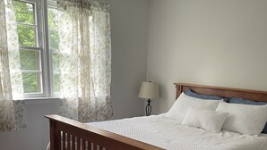 A bedroom with a wooden bed, a bench, a lamp, and a window with curtains.