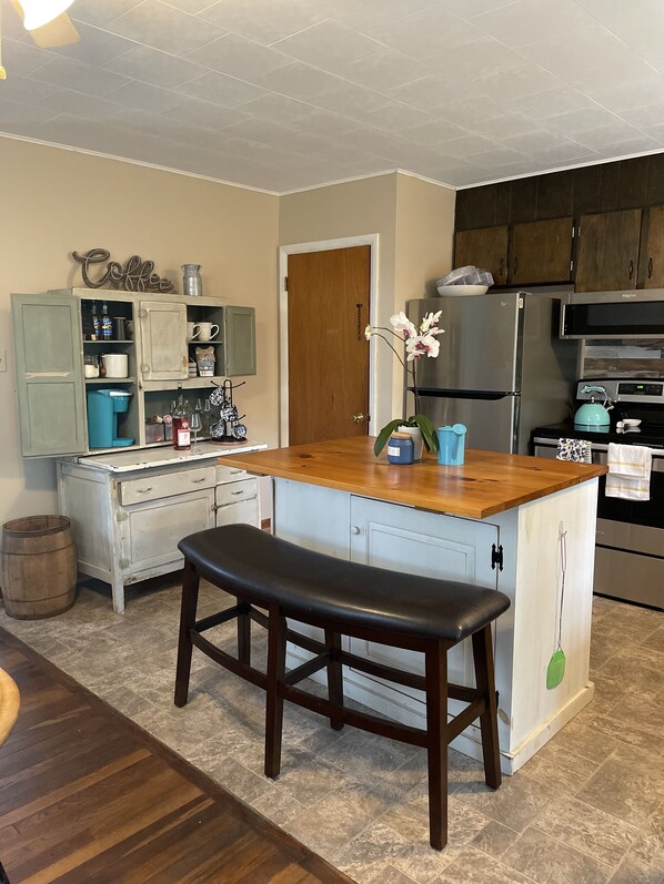 A kitchen with a wooden island, a bench, a refrigerator, and a stove.