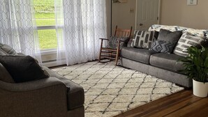 A living room with a grey sofa, a rocking chair, a patterned rug, and a potted plant.