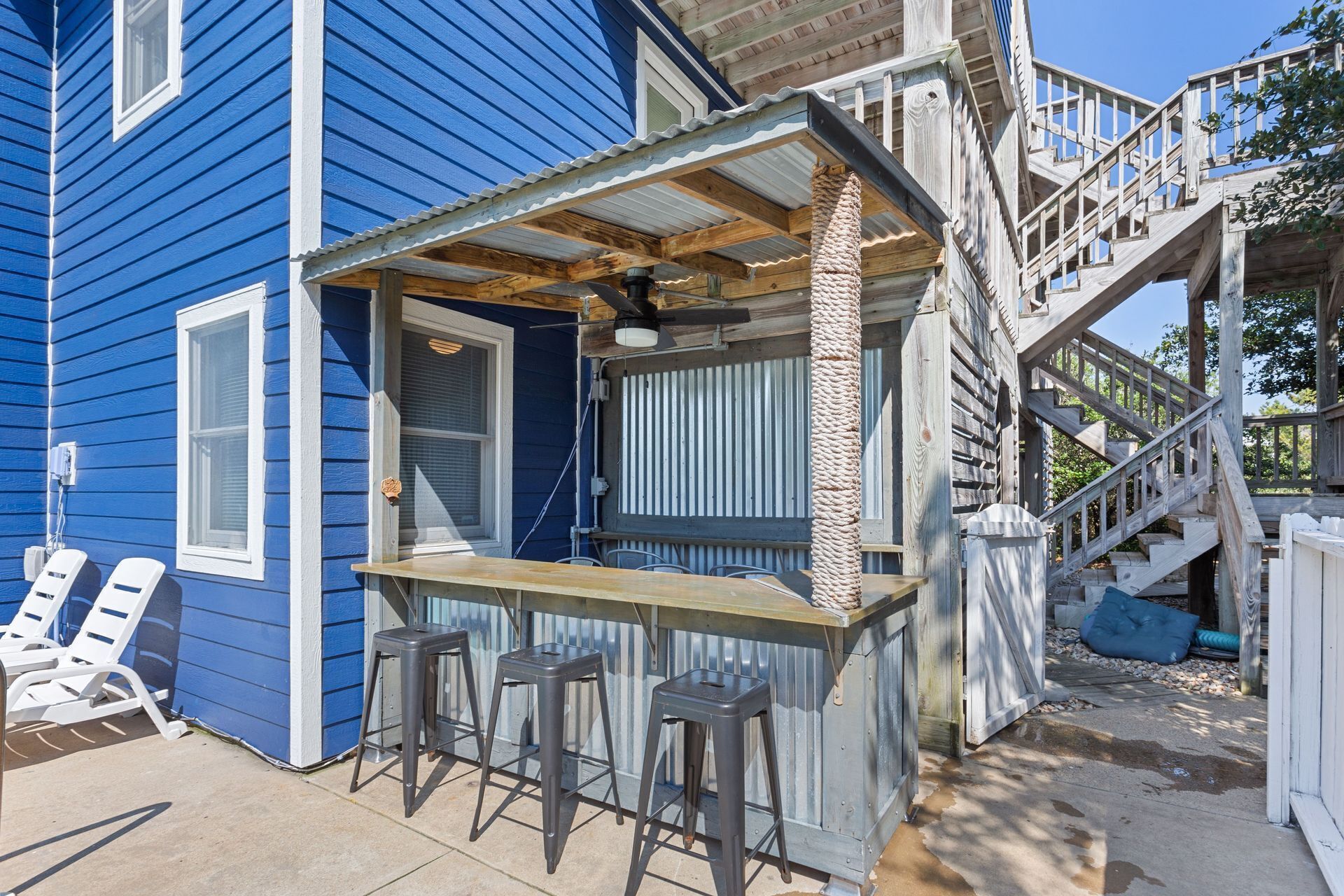 Une maison bleue avec une terrasse en bois, un coin bar avec des tabourets et un escalier menant à un porche abrité.