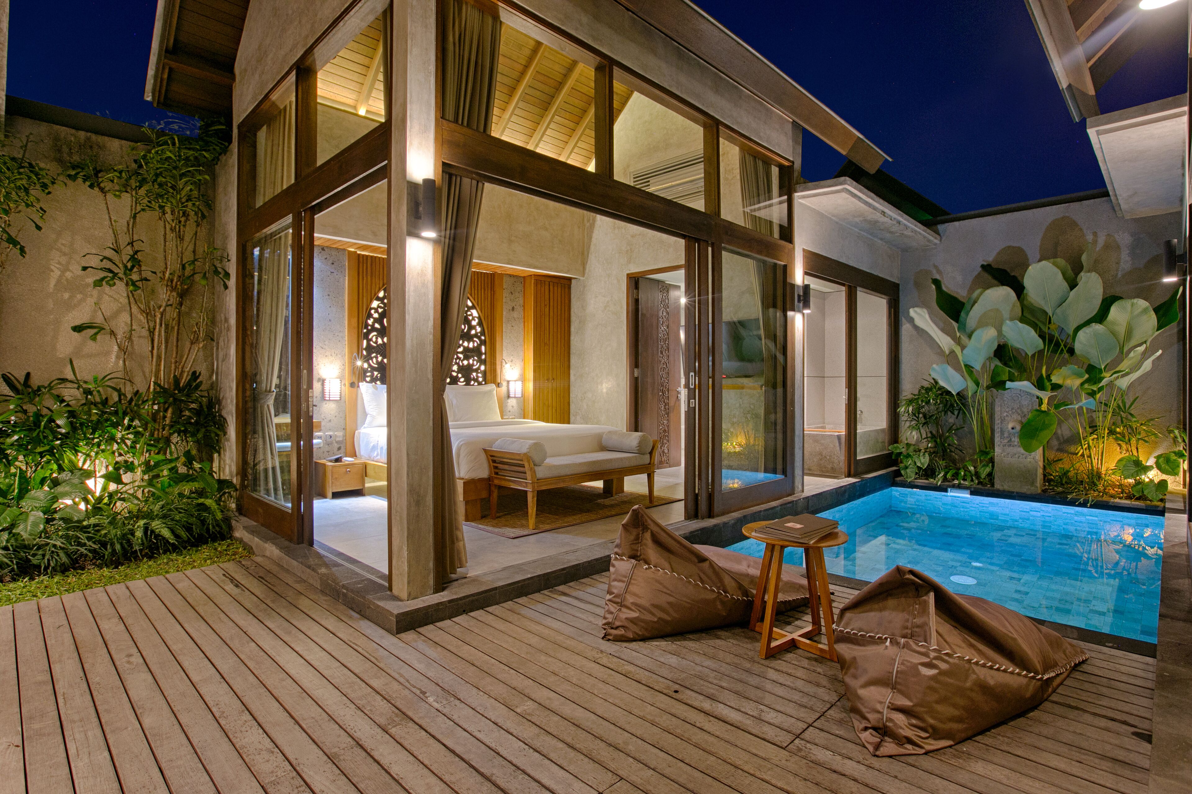 A modern outdoor living area with a pool, wooden deck, and a cozy seating area with cushions.