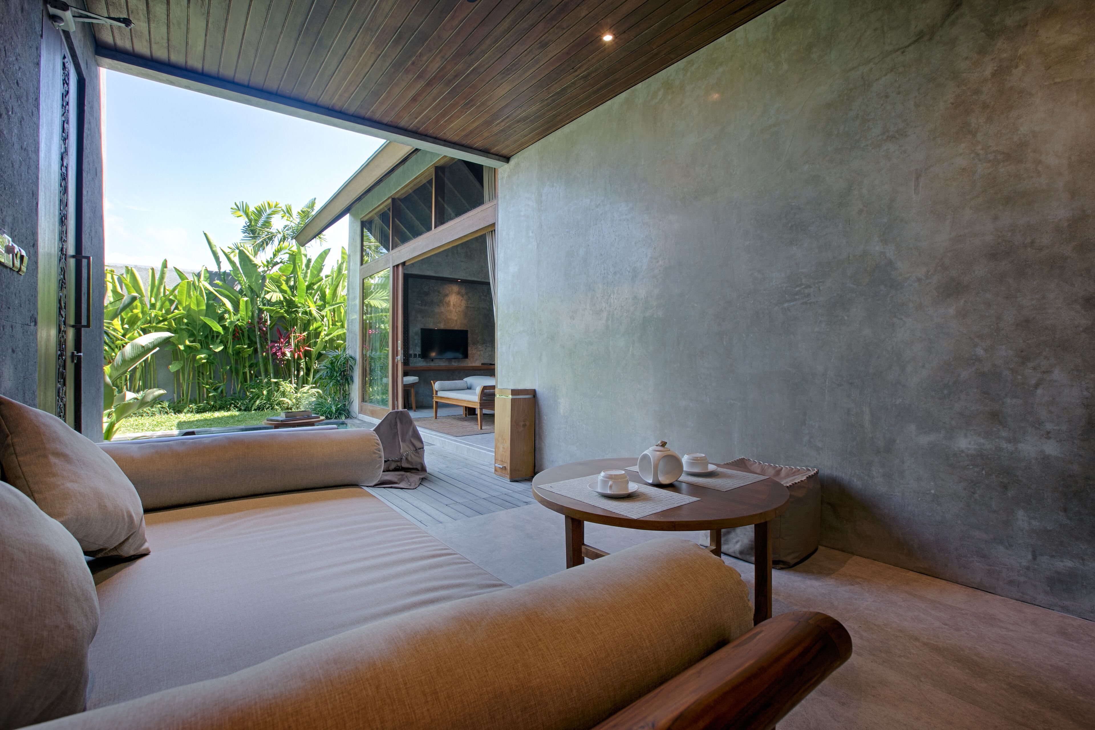 A modern room with a large bed, a small table with tea set, and a view of a garden and outdoor seating area.