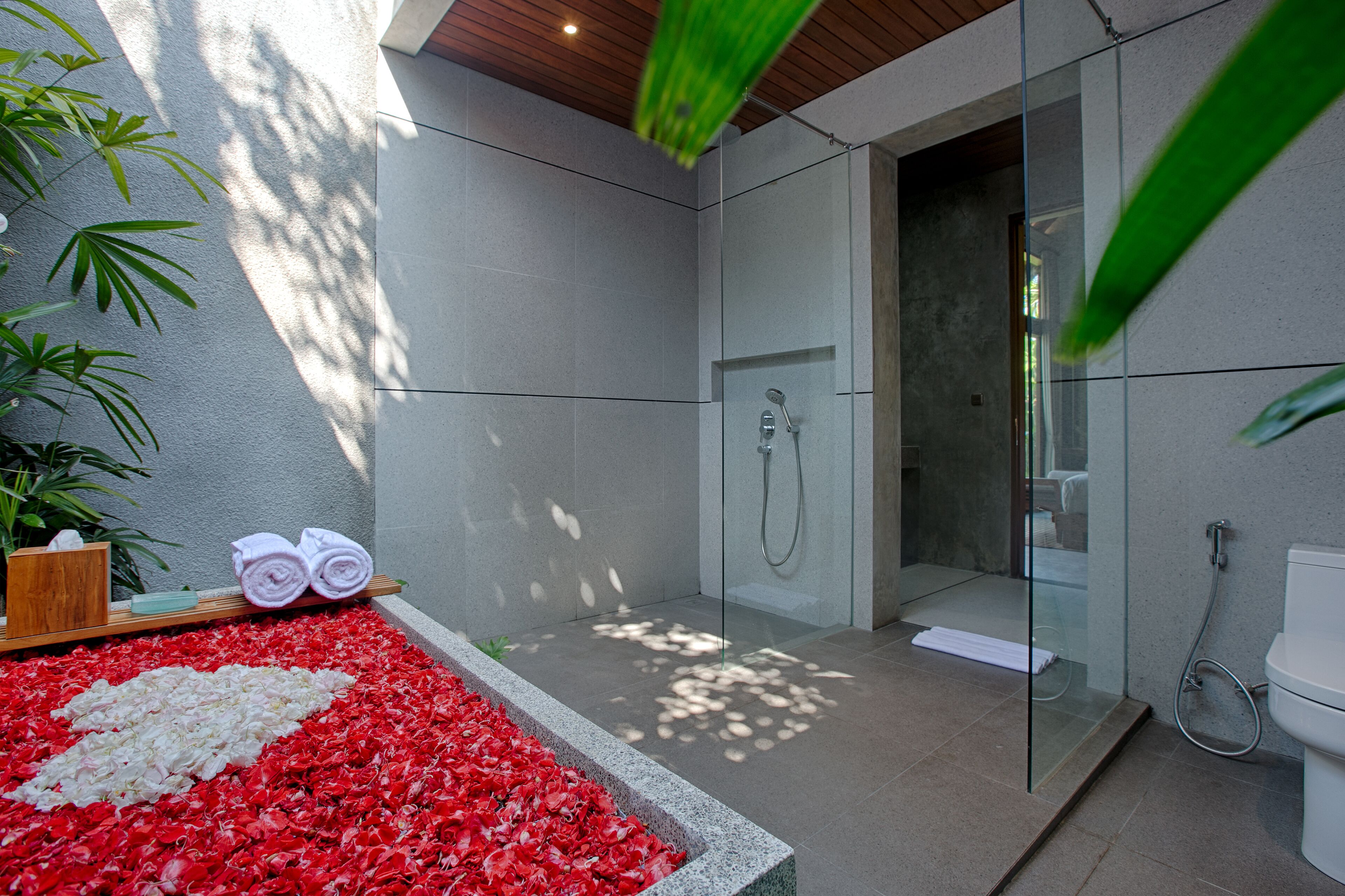 A modern bathroom with a glass-enclosed shower, a toilet, and a bench with towels.
