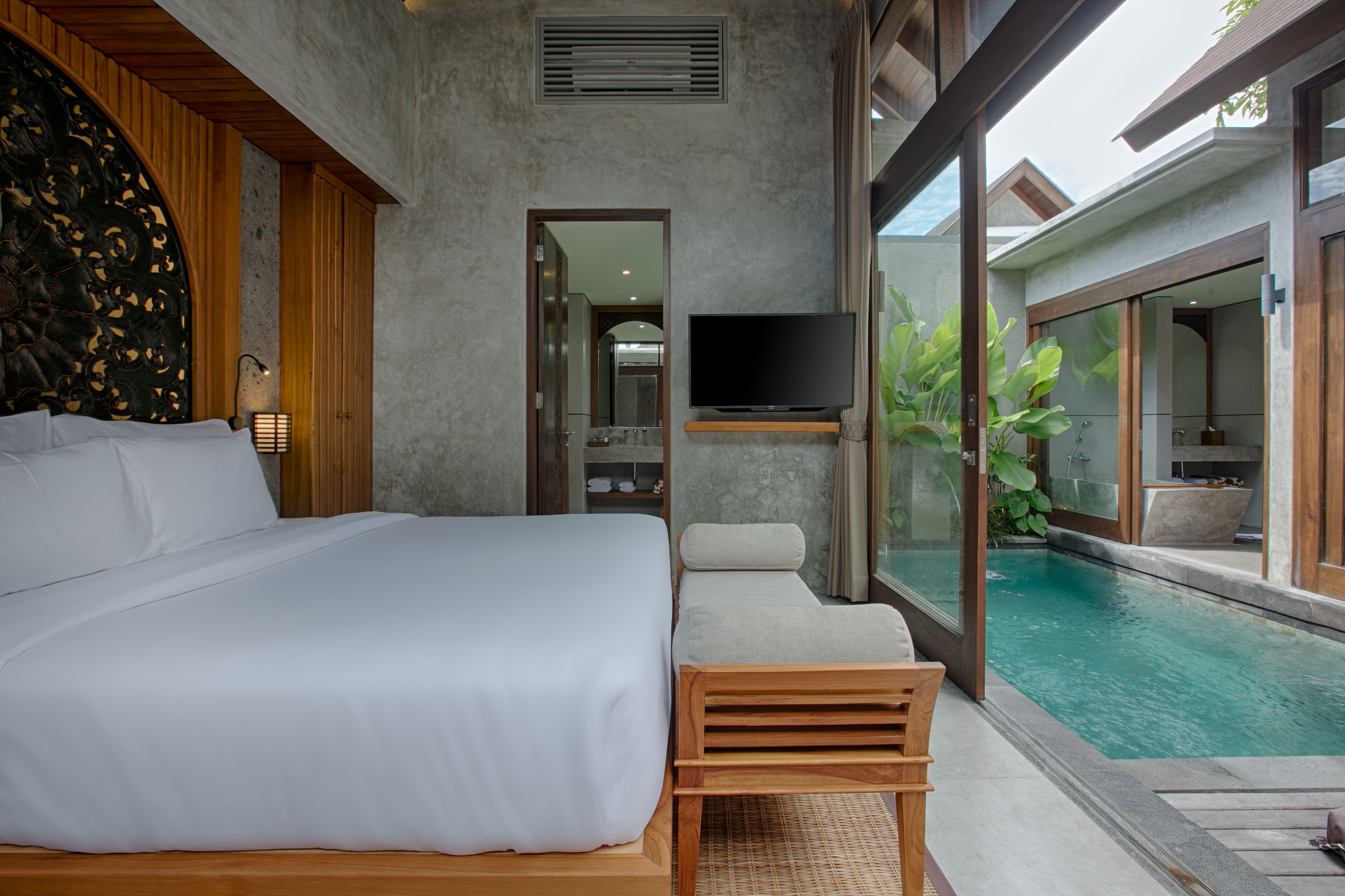 A modern bedroom with a large bed, a TV, and a view of a swimming pool.
