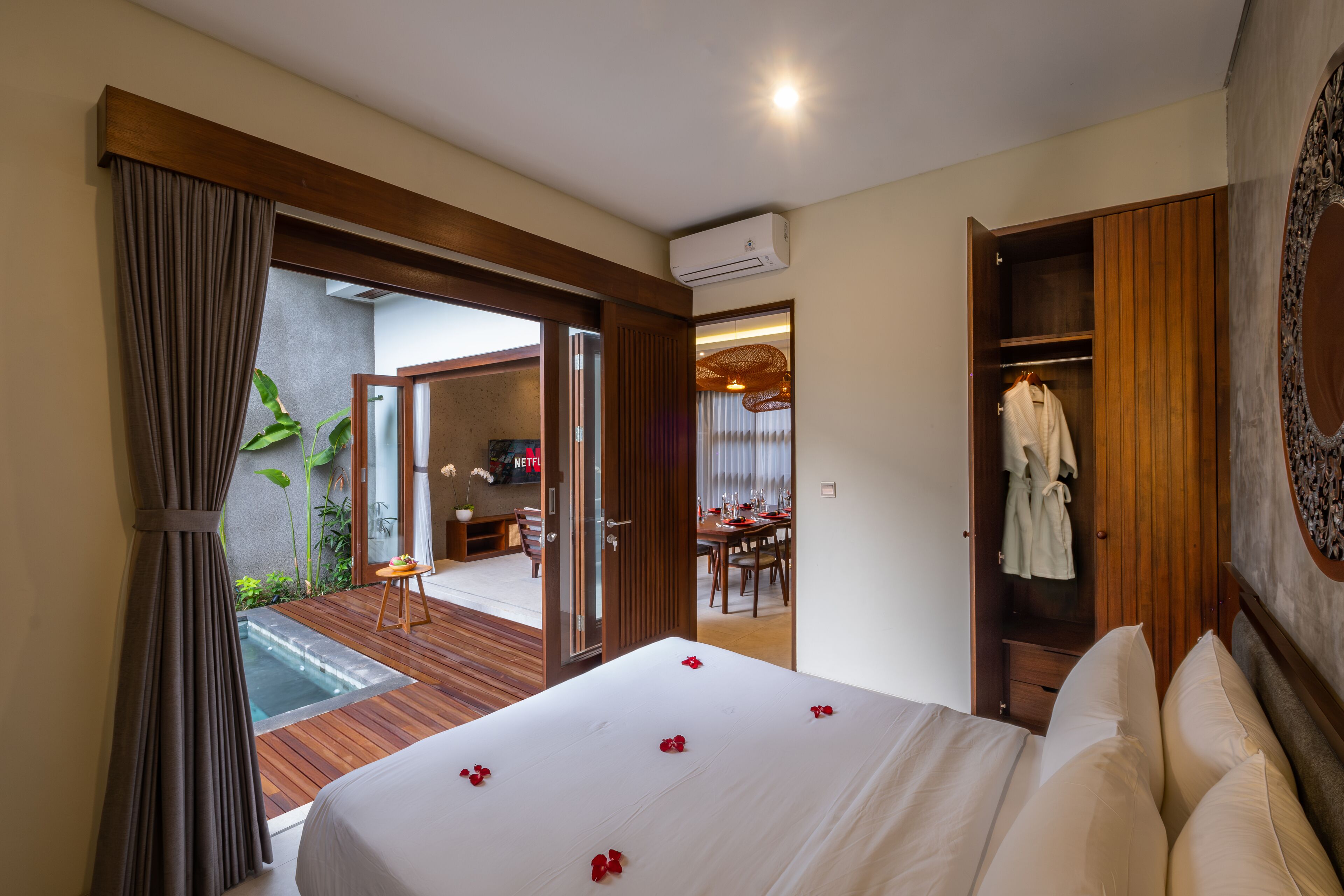 A bedroom with a large bed, a wooden wardrobe, and an open door leading to a dining area.