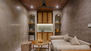 Une pièce de taille modeste avec un plafond en bois, une table ronde sur laquelle sont disposés des fruits, un canapé et un buffet surmonté d’une fenêtre.