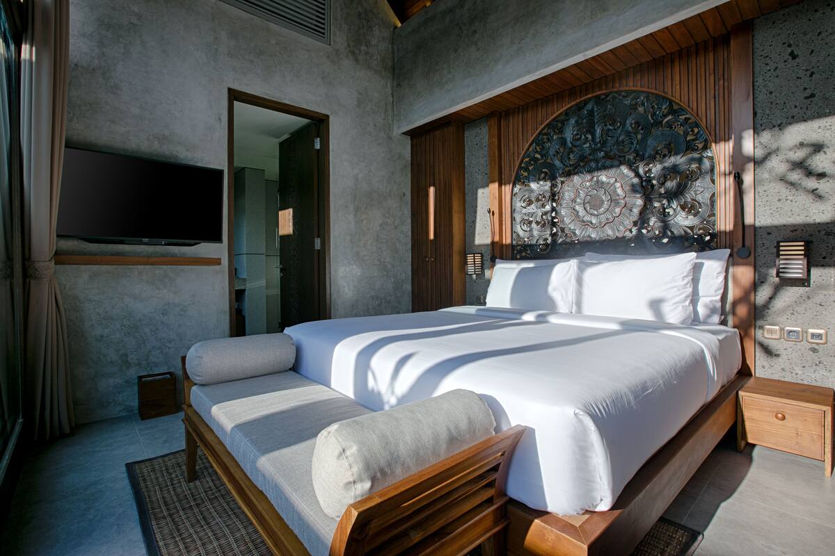 A modern bedroom with a large bed, a flat-screen TV mounted on the wall, and a decorative headboard.