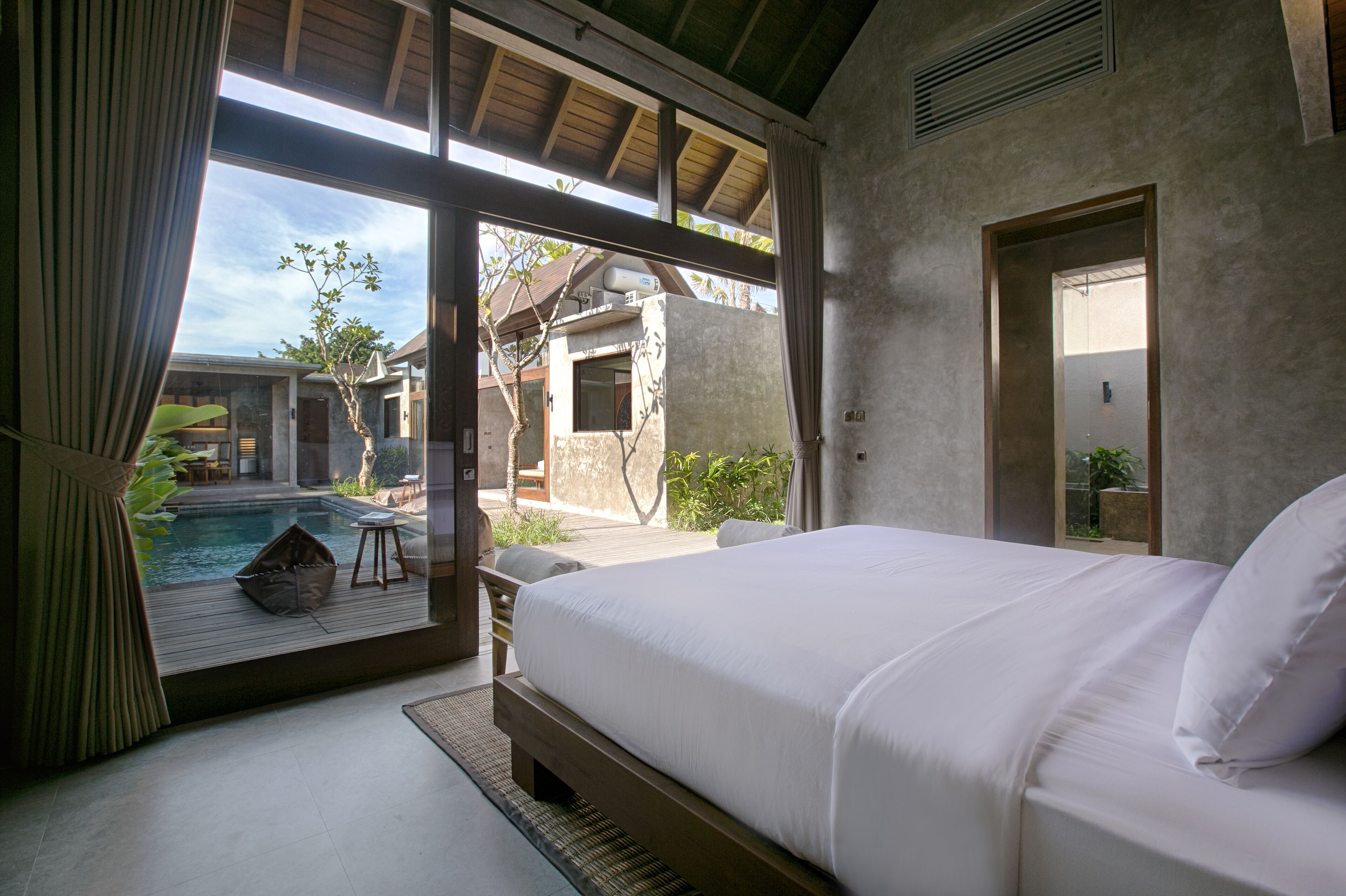 A bedroom with a large bed, a view of a swimming pool, and a door leading to an outdoor area.