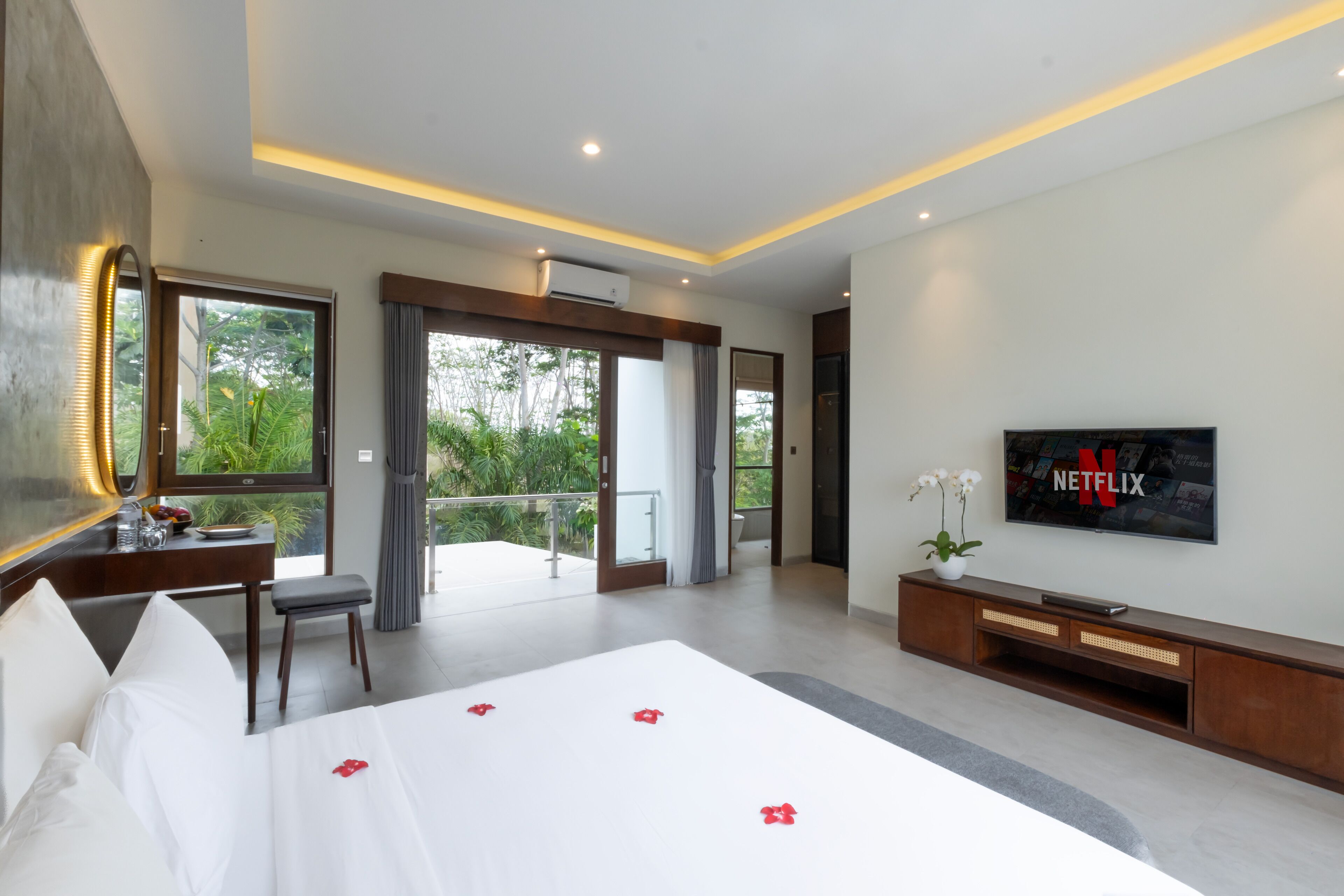 A modern hotel room with a large bed, a TV, and a balcony with a view of greenery.