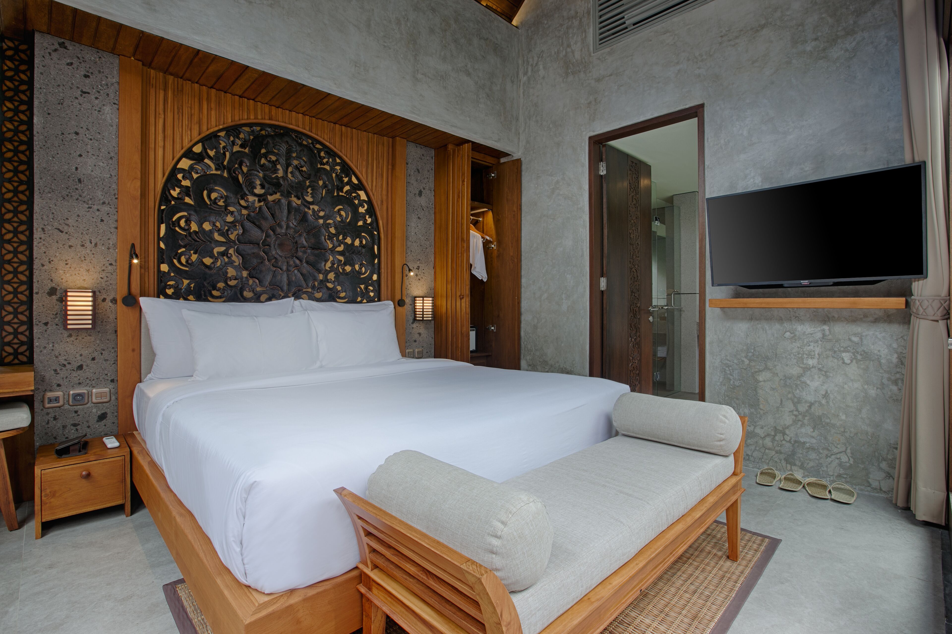 A modern bedroom with a large bed, a wooden headboard, a flat-screen TV, and a small seating area.