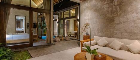 A modern interior with a wooden ceiling, a white sofa, a wooden coffee table, and a large window overlooking a pool area.