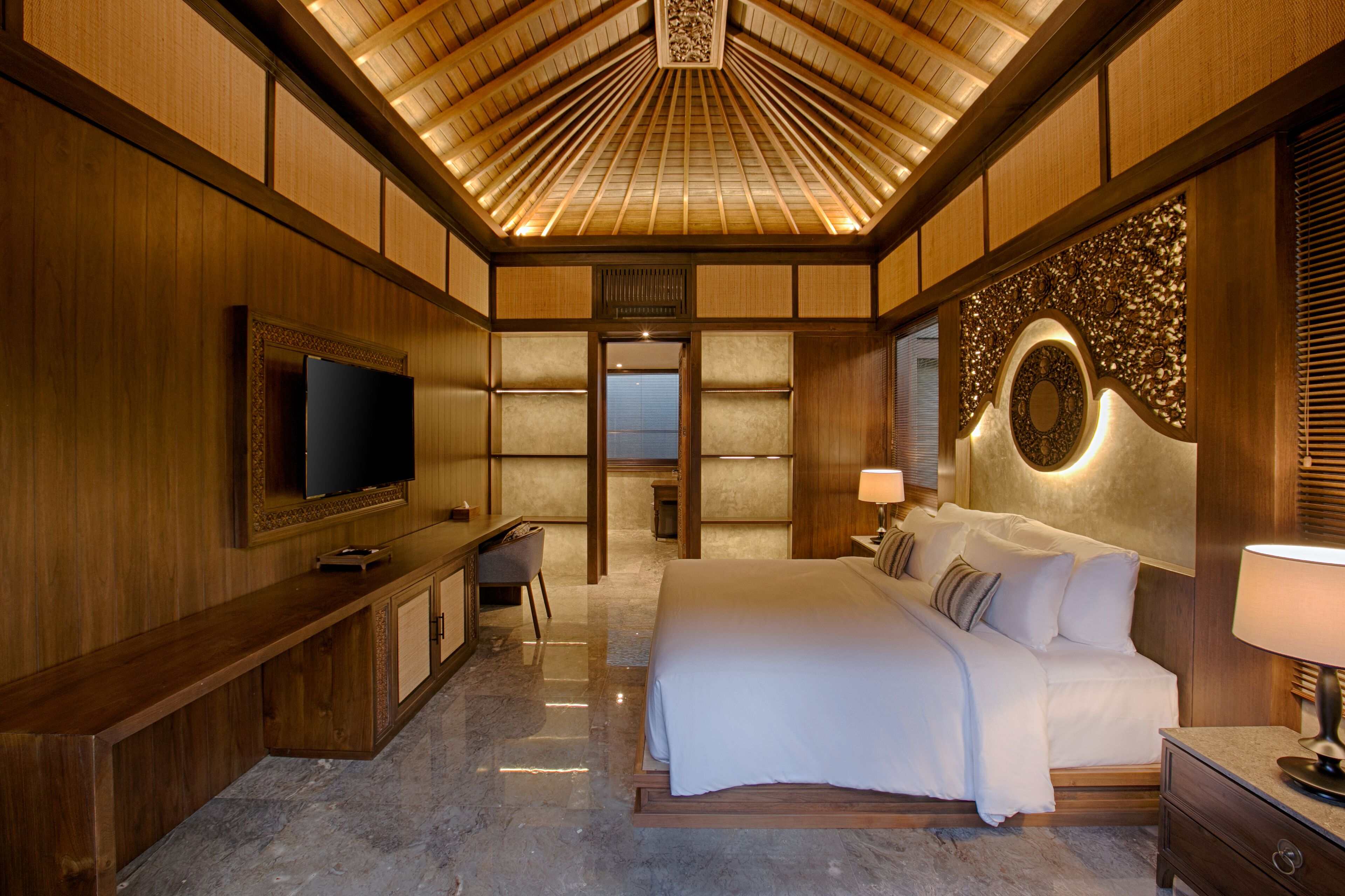 A spacious bedroom with a large bed, a flat-screen TV, a desk, and a chair.