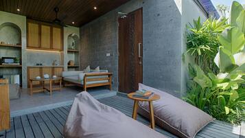 A modern outdoor living area with a wooden ceiling, a sofa, a small table, and a door.