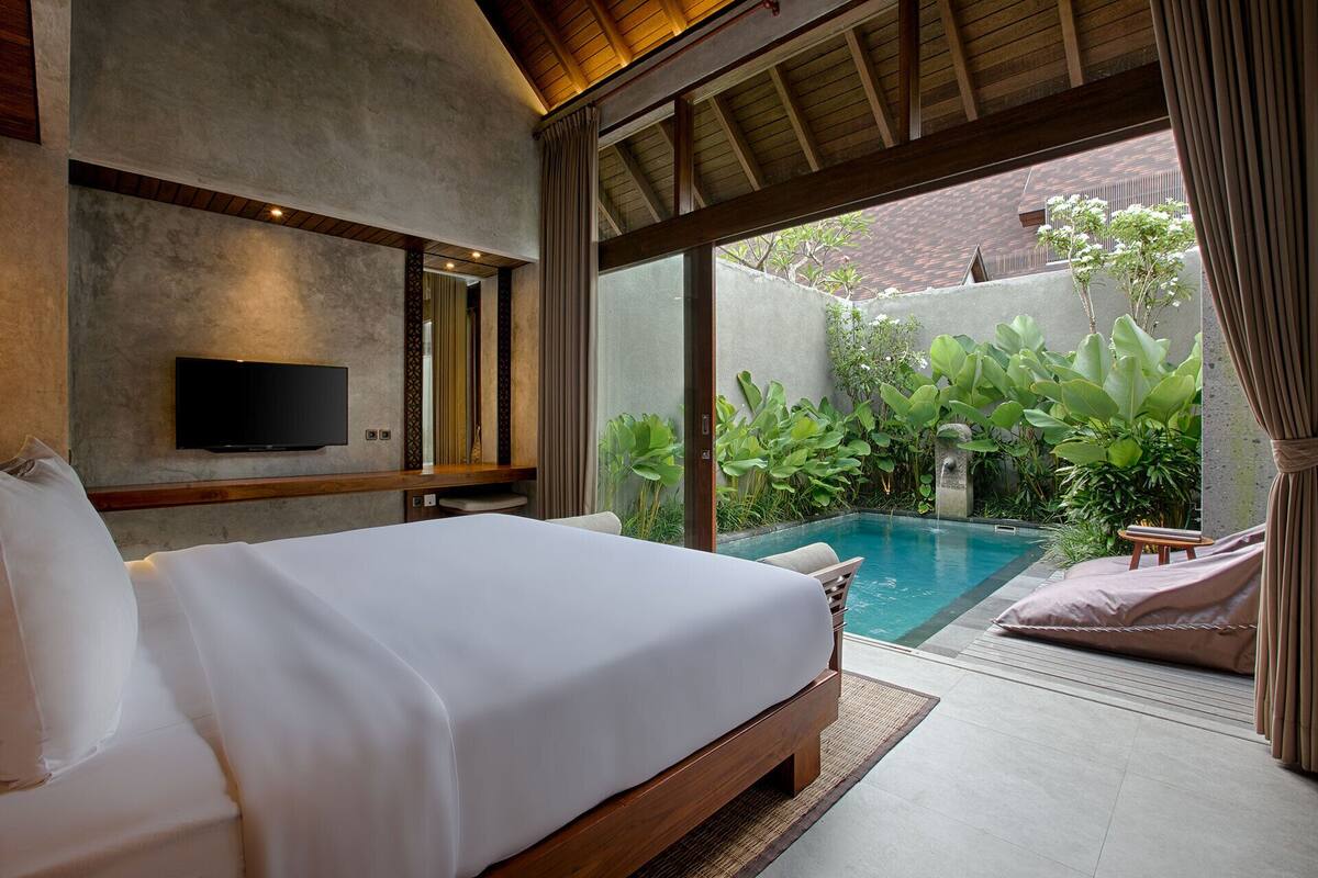 A bedroom with a bed, a TV, and a view of a swimming pool and garden.