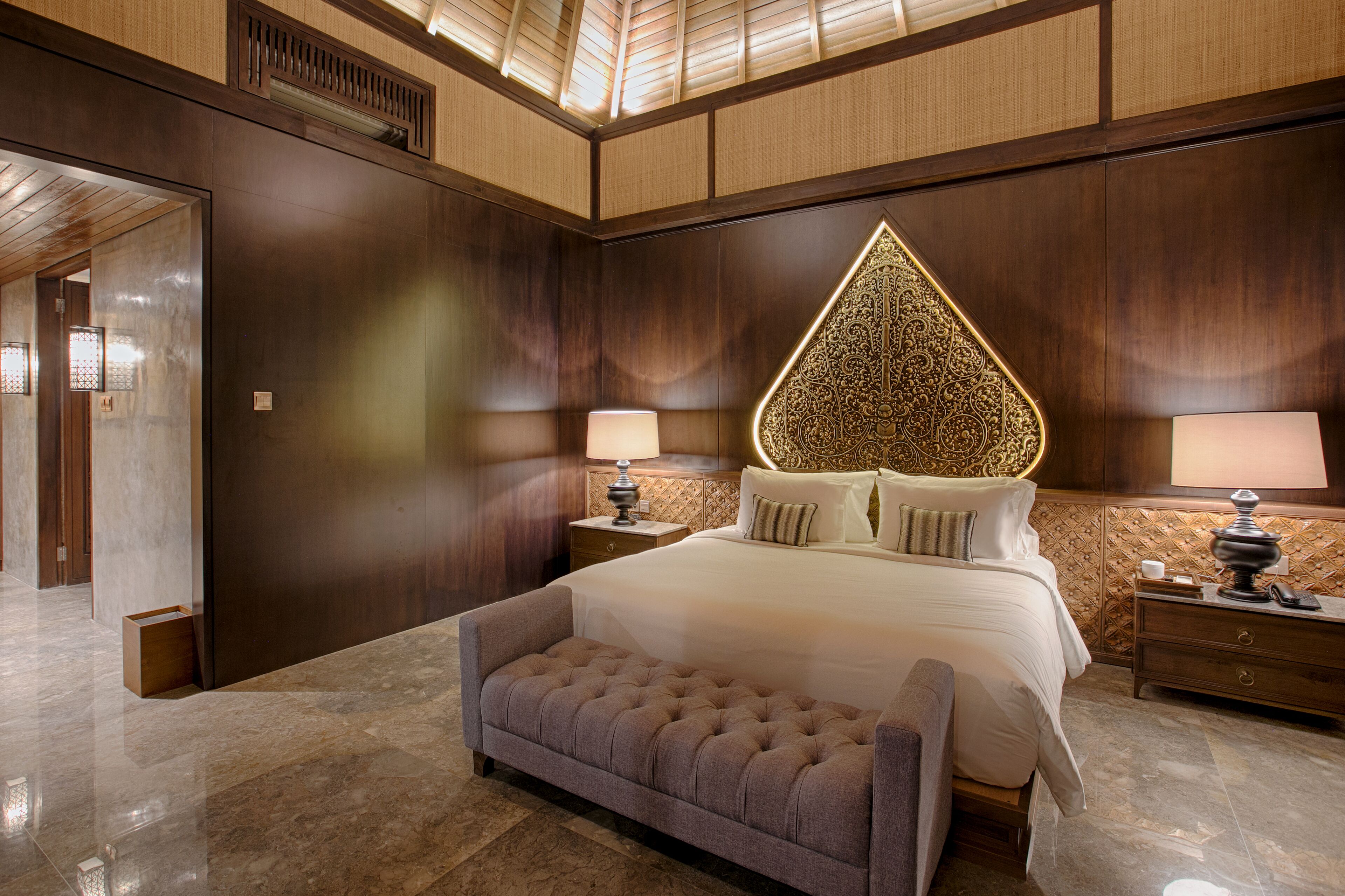 A spacious bedroom with a large bed, a tufted bench, and a decorative wall panel.