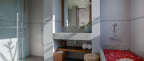 Une salle de bain moderne avec une douche à l’italienne en verre, un lavabo intégré avec un miroir et une baignoire remplie de pétales de roses.