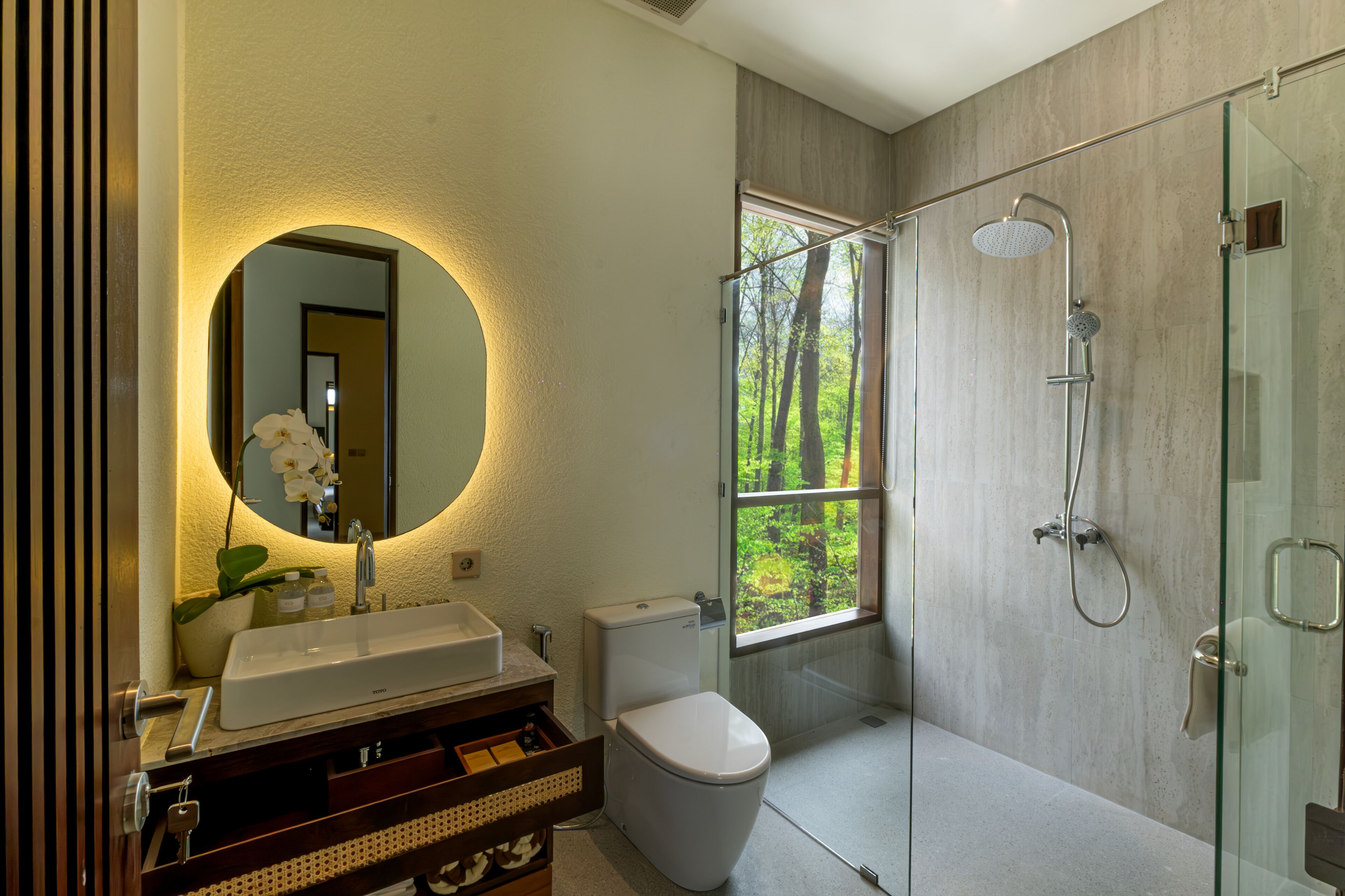 A modern bathroom with a large mirror, a white sink, a toilet, and a glass-enclosed shower.