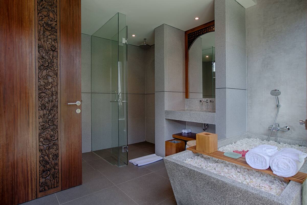 A modern bathroom with a glass shower enclosure, a wooden door with intricate carvings, a granite countertop, and a large mirror.