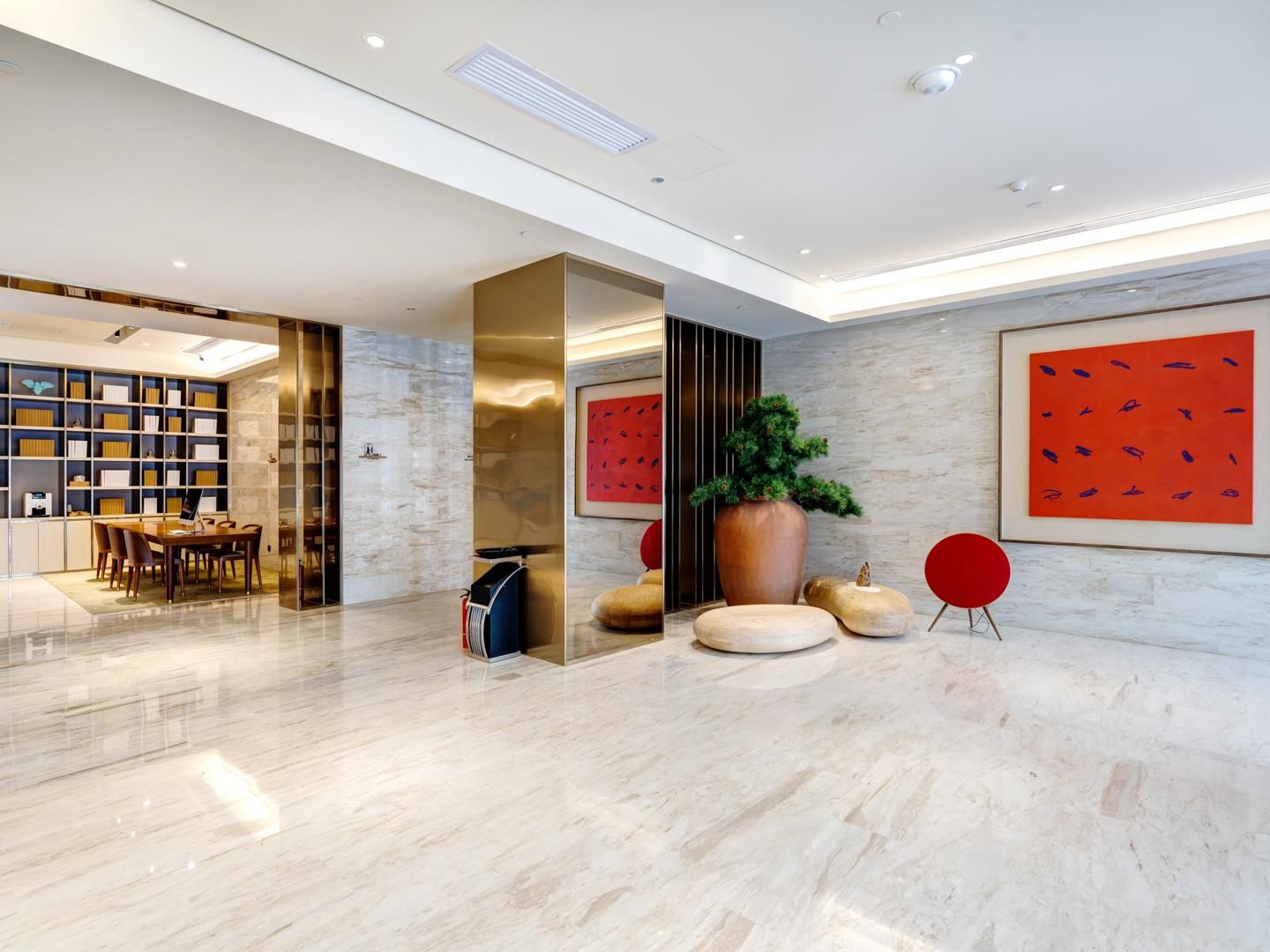 Un vestíbulo moderno con piso de mármol, una zona de estar con una mesa y sillas, una estantería y una planta grande en maceta.