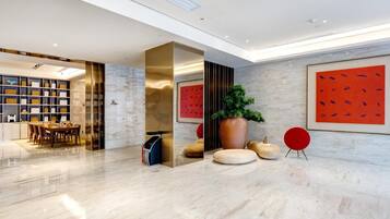 Un vestíbulo moderno con piso de mármol, una zona de estar con una mesa y sillas, una estantería y una planta grande en maceta.