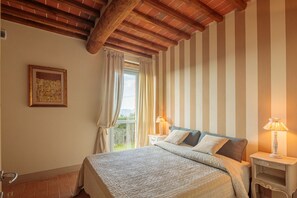Une chambre à coucher avec un lit, des murs à rayures, une fenêtre avec des rideaux, un tableau encadré et une lampe sur une table de chevet.