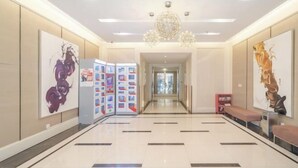 Een ruime lobby met een moderne kroonluchter, een receptiebalie en een digitaal displaypaneel.